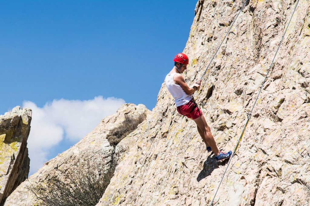 Rock climber ascending a steep cliff surrounded by a vast landscape.