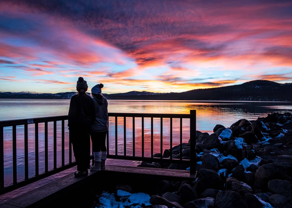 Two silhouetted figures overlooking a colorful sunset landscape.