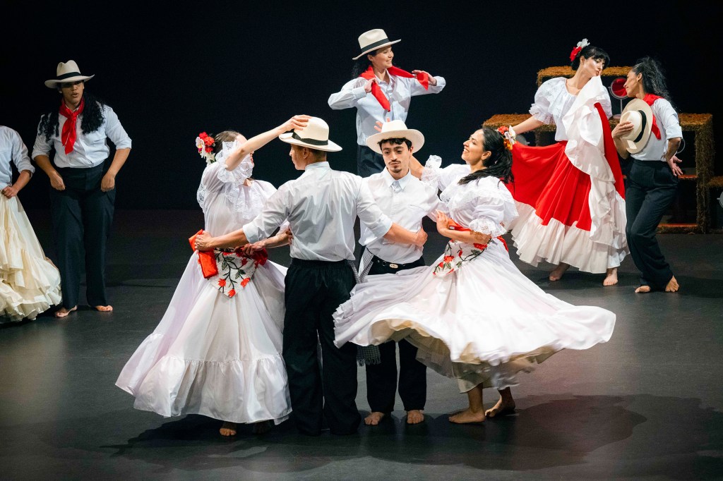 Latin folk dancers performing with traditional textiles on stage.