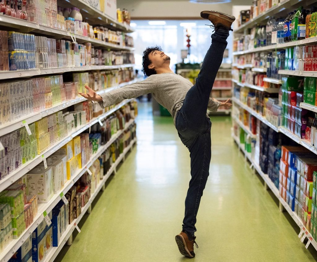 Ballet dancer performing a high leg extension in a supermarket aisle in Toronto.