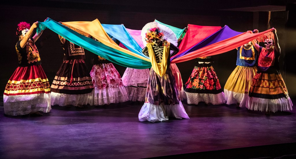 Mexican folk dancers performing with colorful traditional textiles on stage.