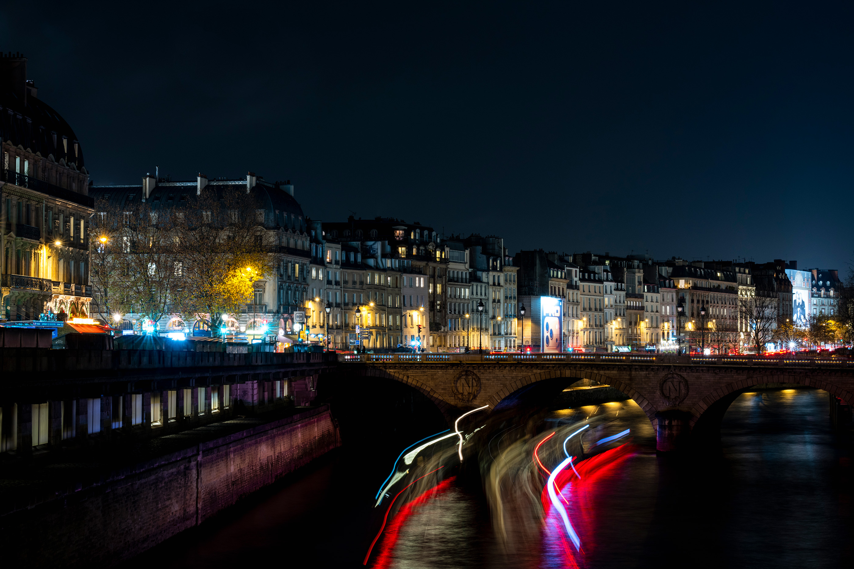 Night view of Paris with light trails beneath a bridge over the Seine.